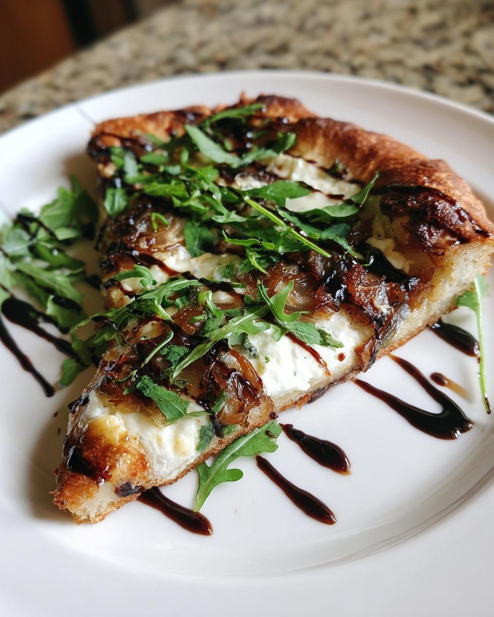 A slice of Goat Cheese Pizza topped with creamy cheese, caramelized onions, fresh arugula, and balsamic glaze on a white plate.