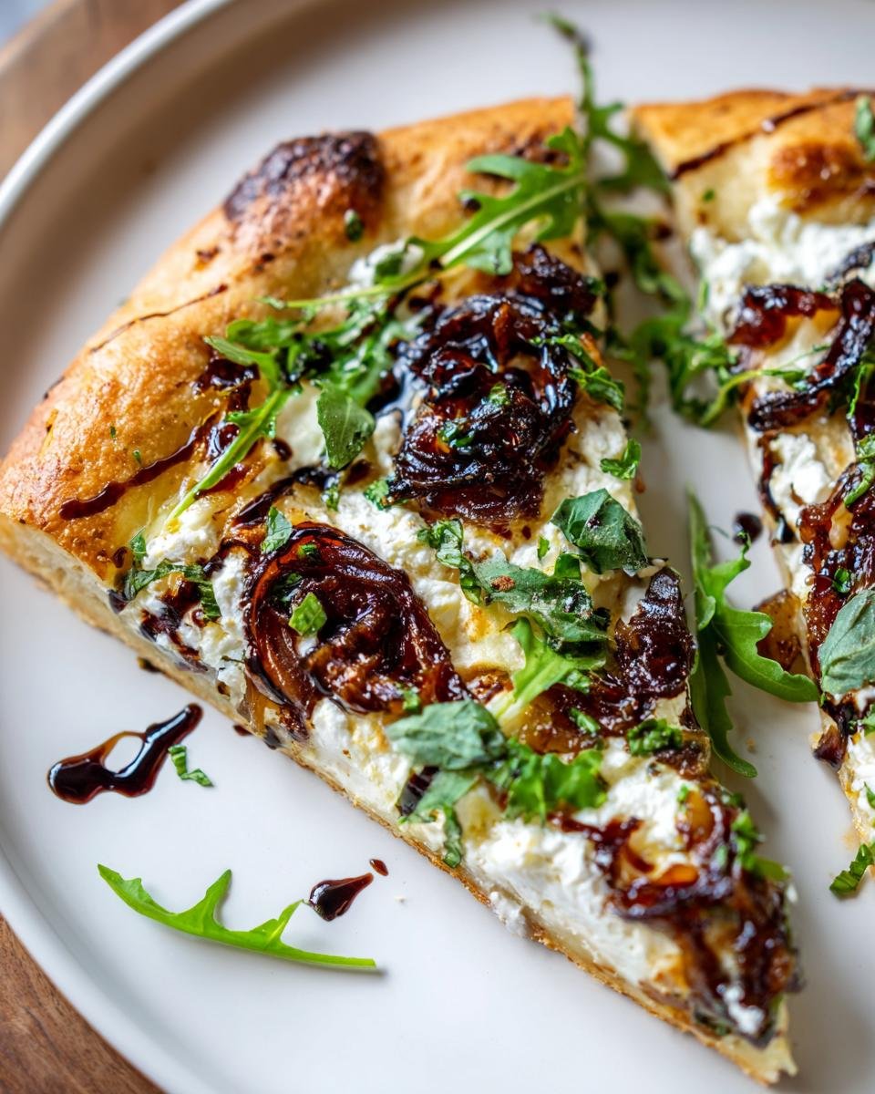 Close-up of a slice of Goat Cheese Pizza topped with creamy cheese, caramelized onions, and fresh arugula.