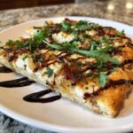 Close-up of two slices of Goat Cheese Pizza topped with caramelized onions, arugula, and balsamic glaze.