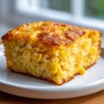 A close-up of a moist, square slice of golden Cornbread Casserole studded with whole kernel corn.