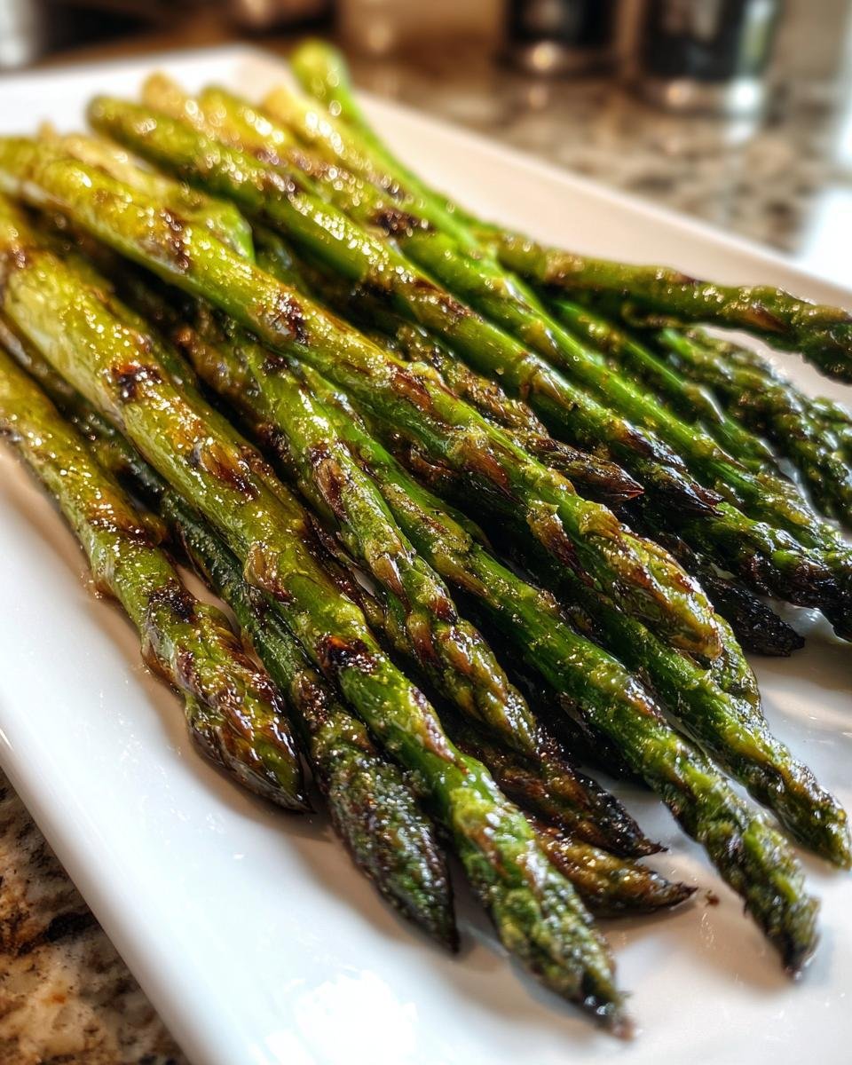 Close-up of bright green, glossy Grilled Asparagus spears with visible char marks, served on a white rectangular plate.