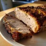 Close-up of a perfectly cooked Grilled Pork Roast, showing a thick slice cut away revealing the moist interior and dark, seasoned crust.