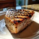 Close-up of a thick, perfectly cooked Grilled Swordfish steak with visible grill marks and black pepper seasoning.