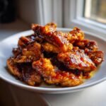 A white plate piled high with crispy, glazed pieces of Honey Garlic Chicken, glistening under natural light.