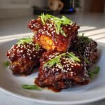 A stack of glossy, dark glazed Instant Pot Sticky Chicken Thighs topped with white sesame seeds and sliced green onions.