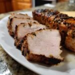 Close-up of sliced Juicy Grilled Pork Tenderloin showing a perfect pink center and charred crust.