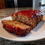 A freshly baked Lipton Onion Soup Meatloaf, sliced to show the texture, covered in a shiny red glaze.