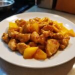 A serving of glossy, saucy Mango Chicken pieces mixed with chunks of bright yellow mango on a white plate.