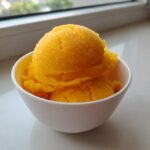 Two scoops of vibrant, icy Mango Sorbet with a slightly crystallized texture, served in a small white bowl.