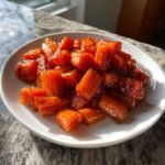A white plate filled with glossy, glazed Maple Roasted Carrots, glistening in natural light.