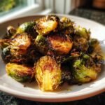 Close-up of crispy, caramelized Oven Roasted Brussels Sprouts piled on a white plate.