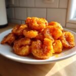 A white plate piled high with crispy, deep-fried Bang Bang Shrimp coated in a vibrant orange, spicy sauce.