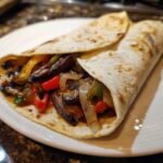 A close-up of a warm tortilla filled with saut&eacute;ed Portobello Mushroom Fajitas, peppers, and onions.