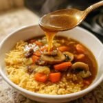 A golden spoon pours thick, savory broth over crispy rice, mushrooms, and carrots in a bowl of Sizzling Rice Soup.