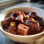 Close-up of tender chunks of Beef Bourguignon stewed in a rich, dark red wine sauce with whole mushrooms.