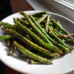 Close-up of perfectly Roasted Green Beans seasoned with garlic and spices on a white plate.