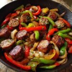 Close-up of browned sausage slices mixed with saut&eacute;ed red, green, and yellow peppers and onions in a Sausage And Peppers Skillet.