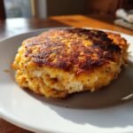 Close-up of a golden-brown, perfectly seared Salmon Burger resting on a white plate.