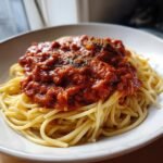 A white bowl filled with spaghetti topped generously with thick, rich Slow Cooker Spaghetti Sauce and dried herbs.