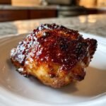 Close-up of a single, perfectly cooked Spicy Sweet Sticky Chicken Thighs piece with a dark, glossy glaze.