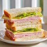 A tall, stacked ham and cheese sandwich with lettuce on white bread, perfect for picnic sandwiches.