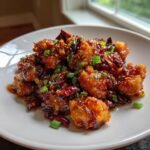 Crispy, glazed pieces of Szechuan Chicken tossed with dried chilies and green onions, served on a light plate.