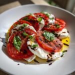 A vibrant Tomato Burrata Salad featuring alternating slices of red tomato and fresh white burrata, drizzled with olive oil and balsamic glaze, topped with basil.