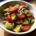 Close-up of a vibrant Avocado Salad featuring diced avocado, halved cherry tomatoes, and sliced red onion tossed in a light dressing.
