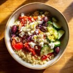 Overhead view of a colorful Mediterranean Bowl featuring quinoa, feta cheese, tomatoes, cucumbers, and olives.