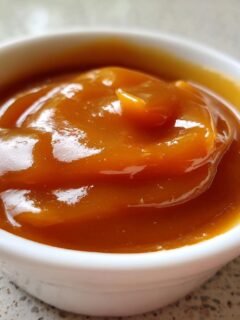A close-up shot of thick, glossy, amber-colored Caramel Dip swirled inside a small white ramekin.
