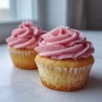Two delicious Strawberry Cupcakes featuring light cake bases and vibrant pink, swirled strawberry frosting.