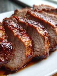 Close-up of sliced Balsamic Roasted Pork Tenderloin with a glossy, dark glaze on a white platter.