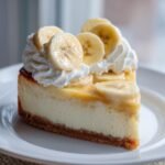 A perfect slice of Banana Cream Cheesecake topped with whipped cream and fresh banana slices on a white plate.