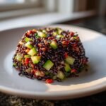 A molded serving of Black Rice Recipes salad mixed with bright green diced cucumber and red peppers.