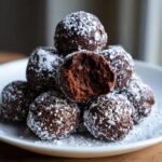 A stack of rich, dark Brownie Truffles dusted heavily with powdered sugar, with one truffle broken open showing the fudgy interior.