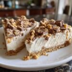 Two slices of creamy, no-bake Butterfinger Desserts on a white plate, topped with chopped candy.