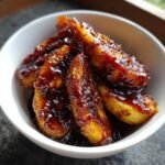 Close-up of thick, glossy sauce coating slices of caramelized bananas served in a white bowl.