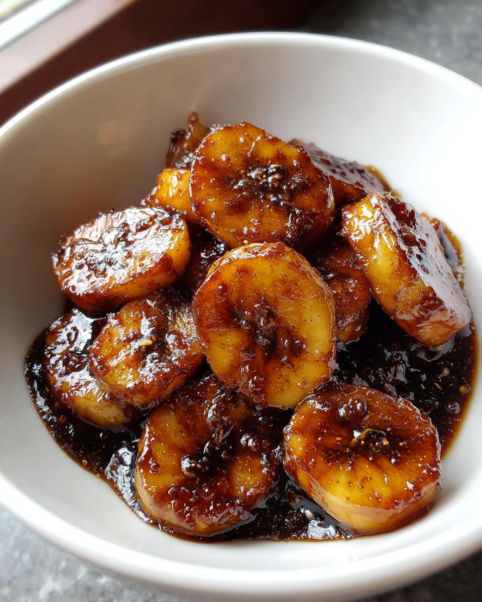 Close-up of thick, glossy Caramelized Bananas slices coated in a dark, rich sauce inside a white bowl.