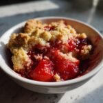 A close-up of a serving of warm Cherry Cobbler With Cake Mix, featuring bright red cherry filling and a crumbly topping in a white bowl.