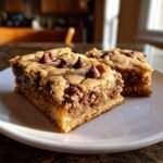 Two thick, chewy squares of Chocolate Chip Blondies loaded with melted chips, served on a white plate.