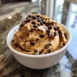 A close-up of thick Chocolate Chip Cookie Dough Dip topped generously with mini chocolate chips in a white bowl.