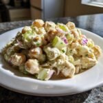 A close-up of creamy Chickpea Salad mixed with celery and red onion served on a white plate.