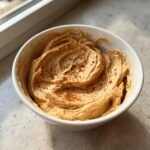 A close-up of creamy, spiced Monkey Butter swirled in a white bowl and dusted with cinnamon.