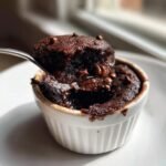 A spoonful of warm, gooey Chocolate Cobbler topped with melted chocolate chips being lifted from a white ramekin.