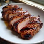 Close-up of perfectly cooked, sliced Grilled Pork Tenderloin with a caramelized, dark glaze on a white plate.