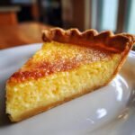 Close-up of a golden-brown slice of Lemon Chess Pie with a creamy yellow filling on a white plate.