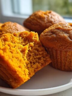 Close-up of moist, bright orange Pumpkin Muffins, one broken open to show the crumb texture.