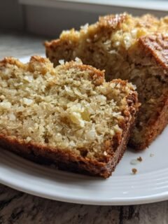 Two thick slices of moist Pineapple Quick Bread showing visible chunks of fruit, served on a white plate.