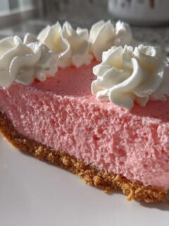A close-up slice of bright pink Pink Lemonade Pie with a graham cracker crust and topped with swirls of whipped cream.