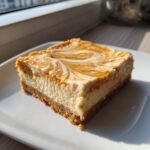 A single square slice of Pumpkin Cheesecake Bars showing a graham cracker crust, creamy filling, and a pumpkin-vanilla swirl topping.